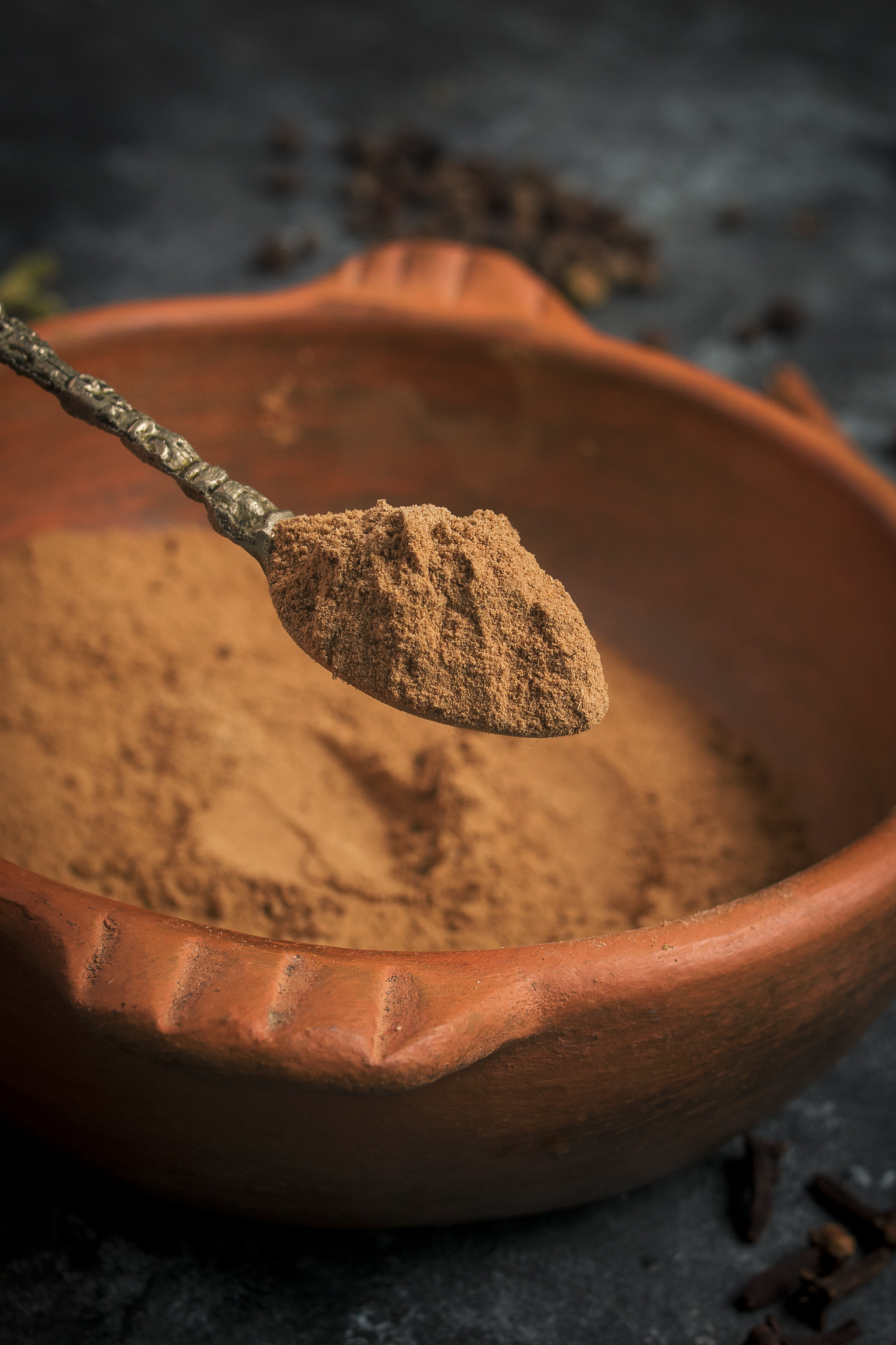 Spoonful of homemade pumpkin pie spice held above a terracotta bowl of the finished blend.
